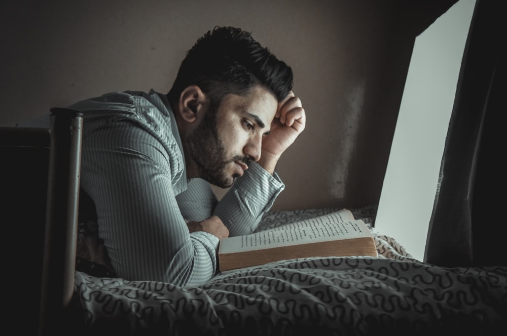 man lying on bed while reading book