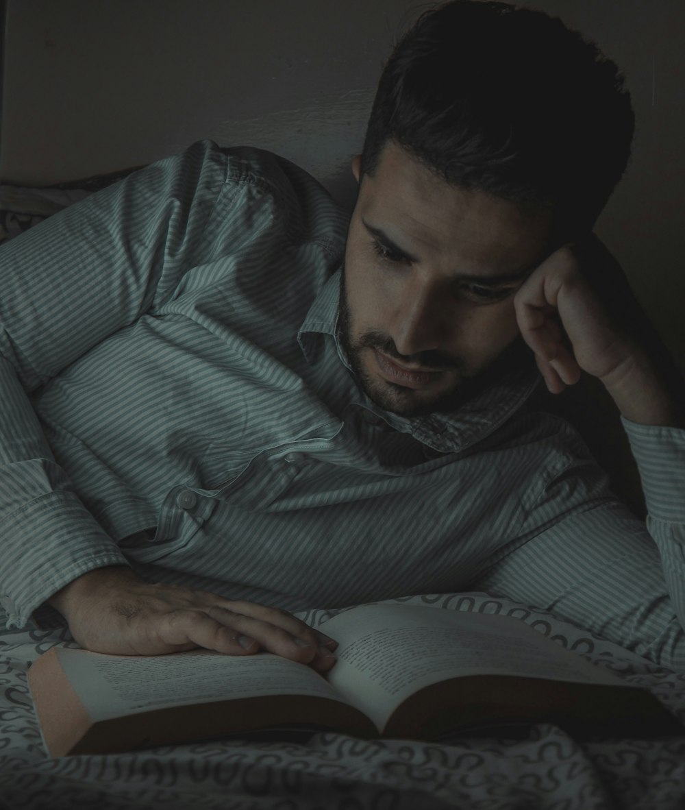 man reading book while lying on bed