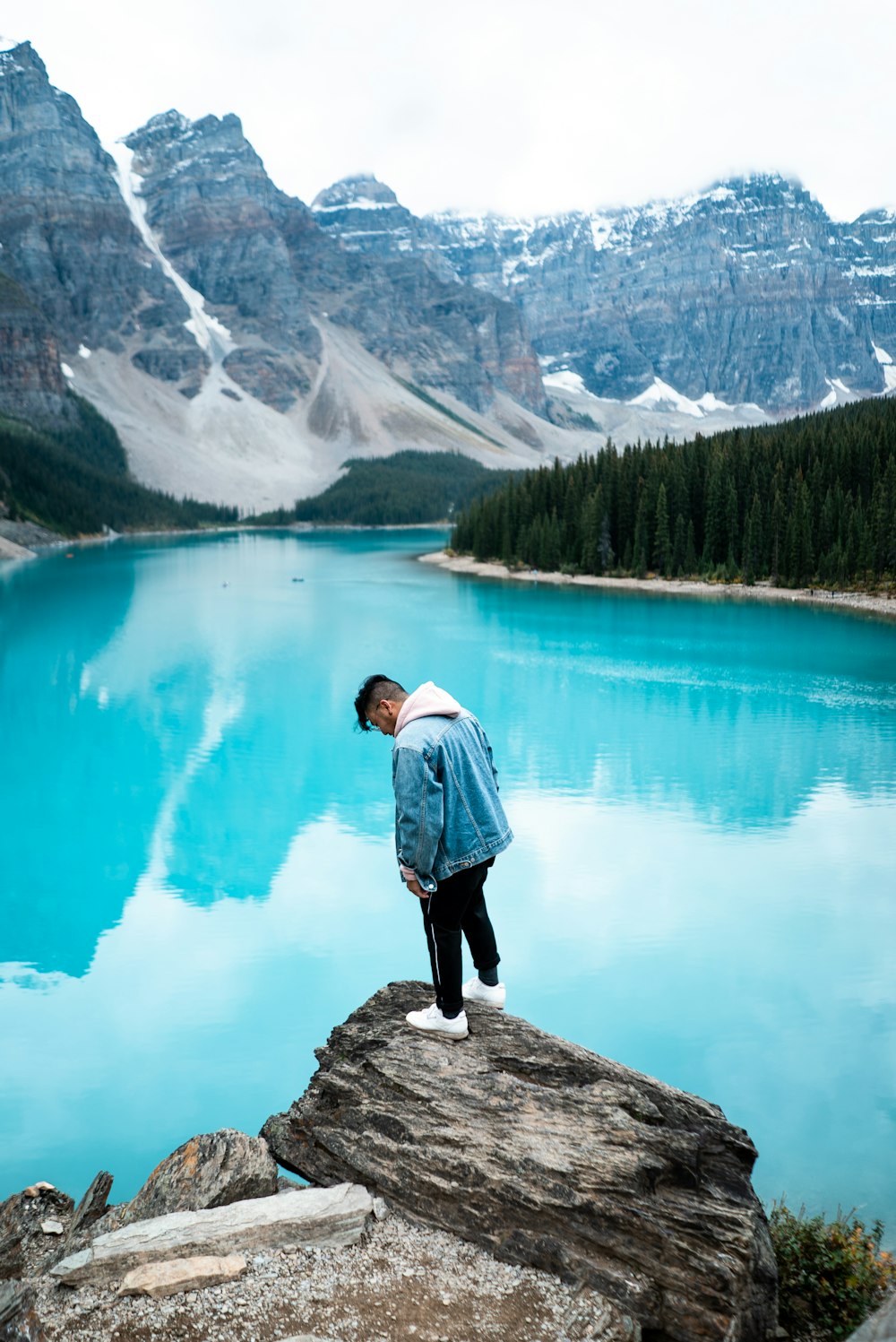 man standing on rocky mountain near clear body of water