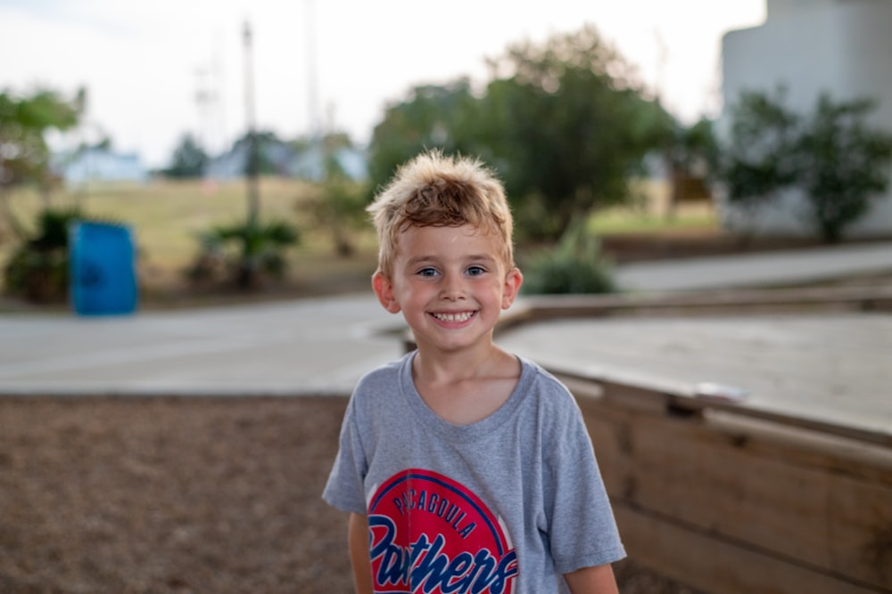 Fotografia de foco seletivo do menino sorridente na camisa cinza durante o dia