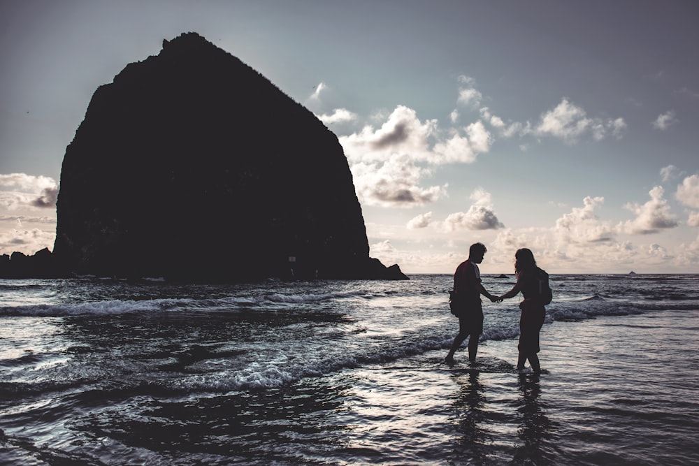 silhouette of man and woman standing beside seashore during daytime