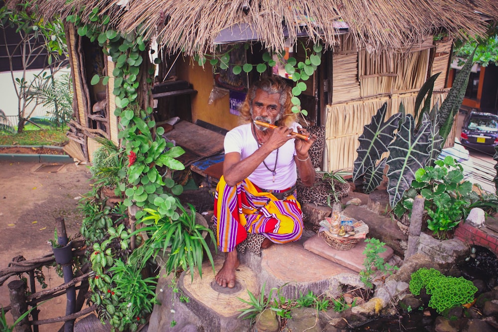 man playing wooden flute sitting beside house