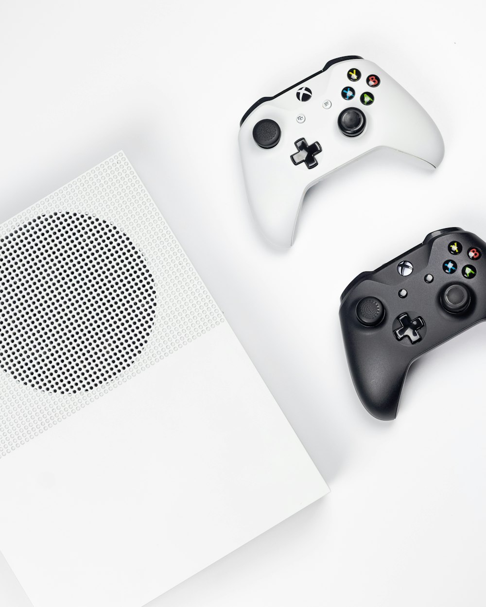 white Xbox One and two black and white game controllers on white background