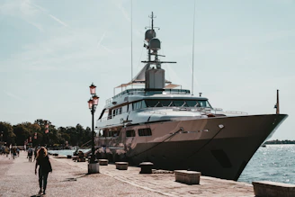 A custom luxury yacht docked at a sunlit harbor with workers preparing it for launch.