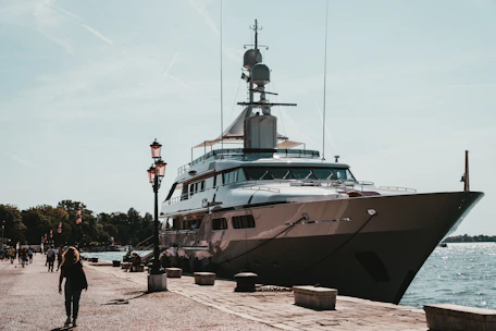 A custom luxury yacht docked at a sunlit harbor with workers preparing it for launch.