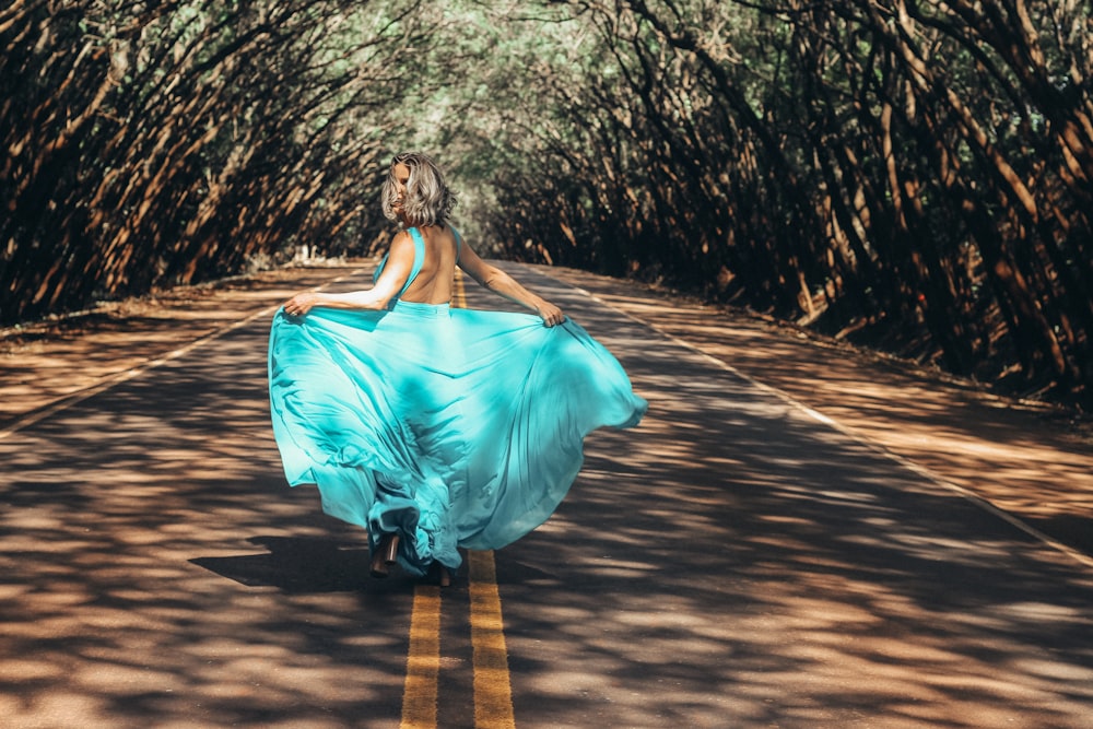 femme portant une robe dos nu turquoise marchant sur une route asphaltée