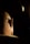 A close-up view of the back of a person's bald head with one ear highlighted by dramatic lighting. The surrounding environment is dimly lit, creating a strong contrast between light and shadow.