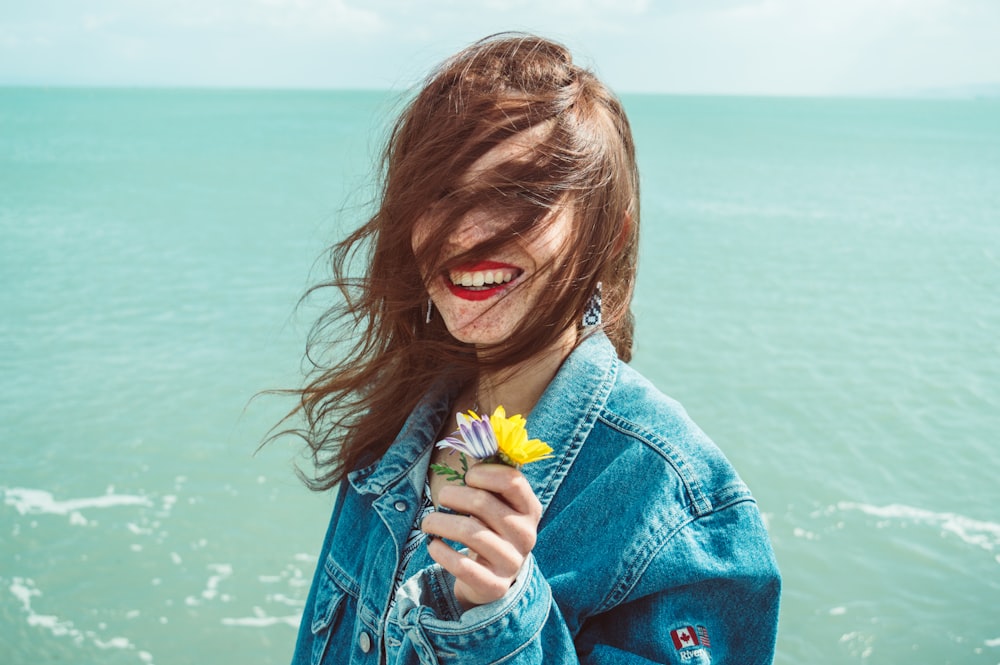 smiling woman holding yellow flowers in front of sea