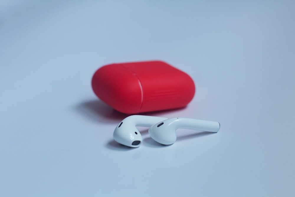 white wireless earbuds with red charging case on white surface