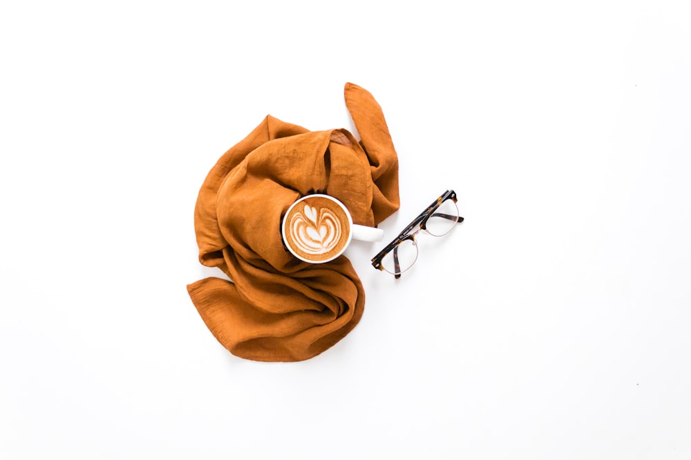 ein Schal, eine Brille und eine Tasse Kaffee auf einer weißen Oberfläche
