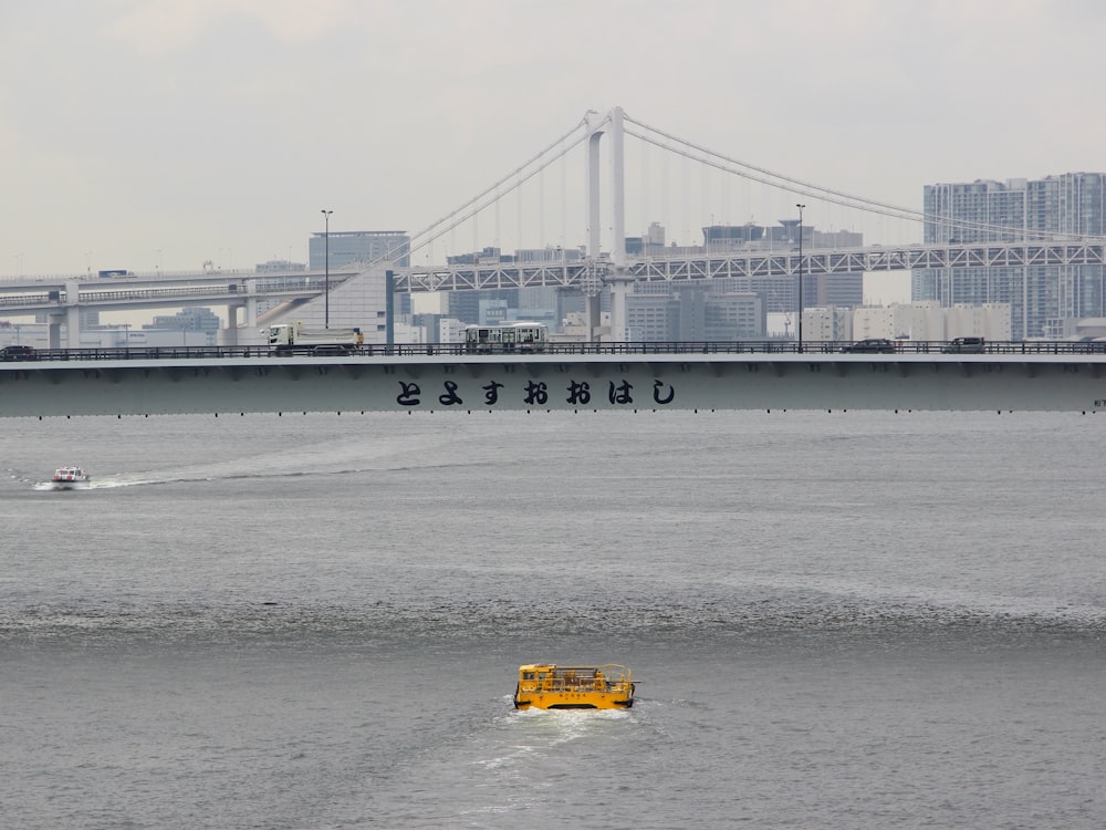 yellow motorboat on sea water near grey metal bridge