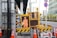 A street scene featuring a construction site with orange traffic cones and a digital sign displaying a construction worker icon and caution symbols in the foreground, set against an urban backdrop with high-rise buildings.