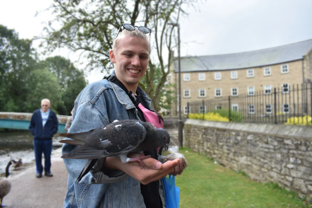 A smiling customer holding a pigeon with a backdrop of green fields and blue sky.