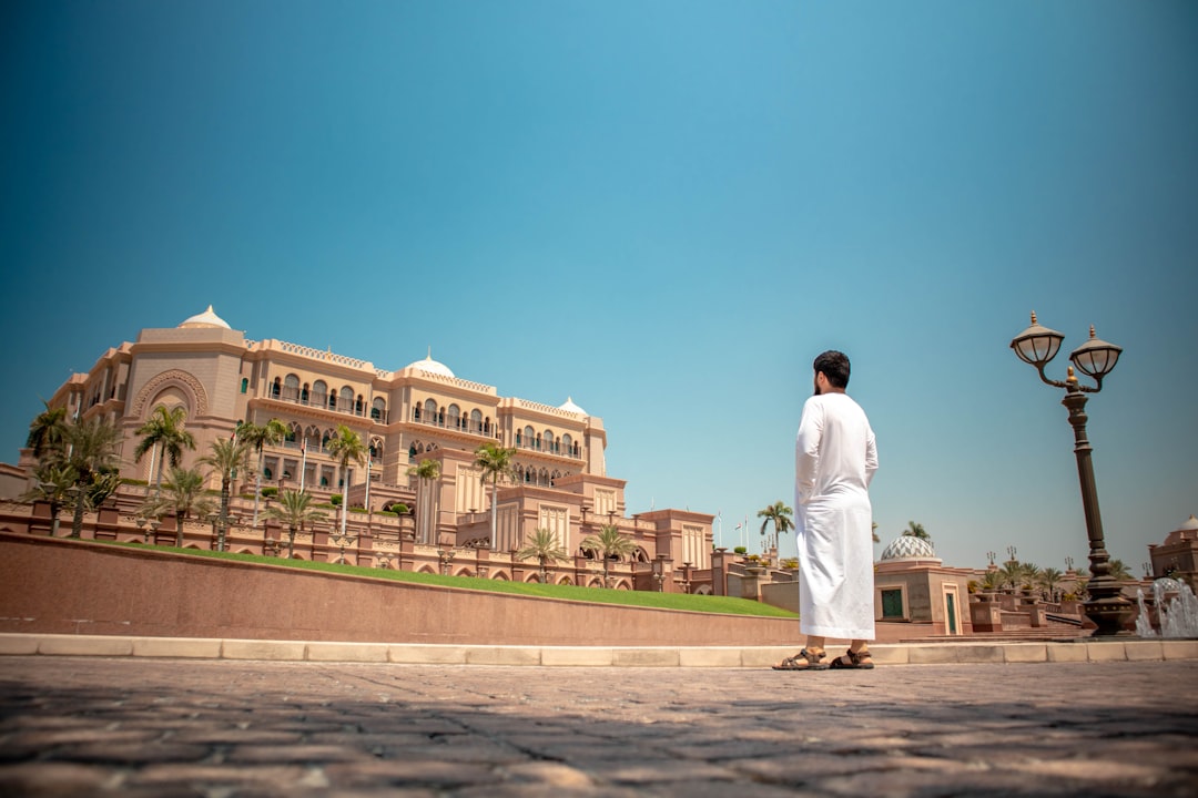 man in white tunic standing in front of mansion