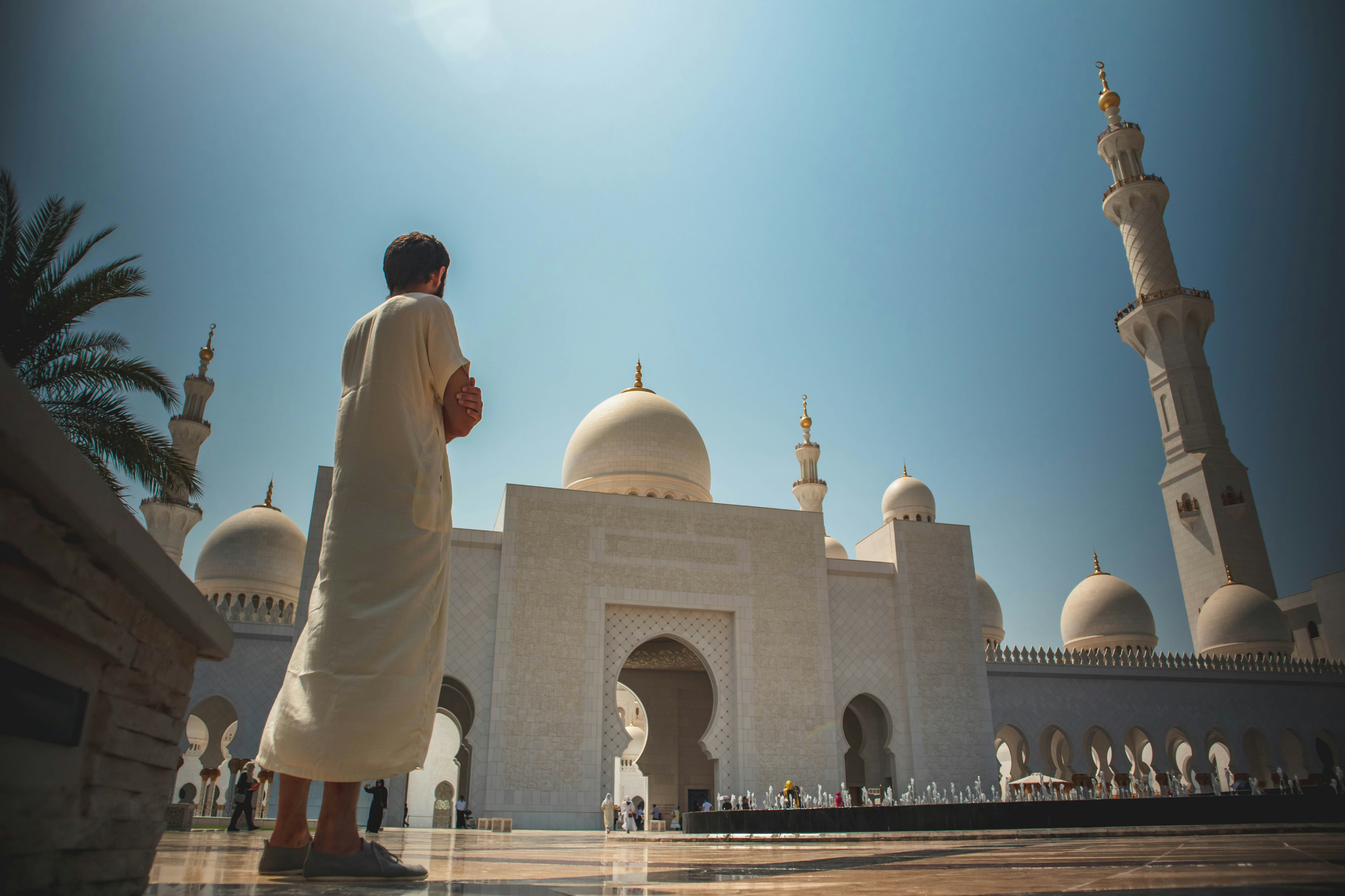 A wide shot of a person wearing white thawb standing at Sheikh Zayed Grand Mosque Center in Abu Dhabi
