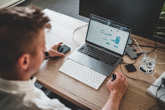 man holding mouse and iPhone while using Macbook Pro