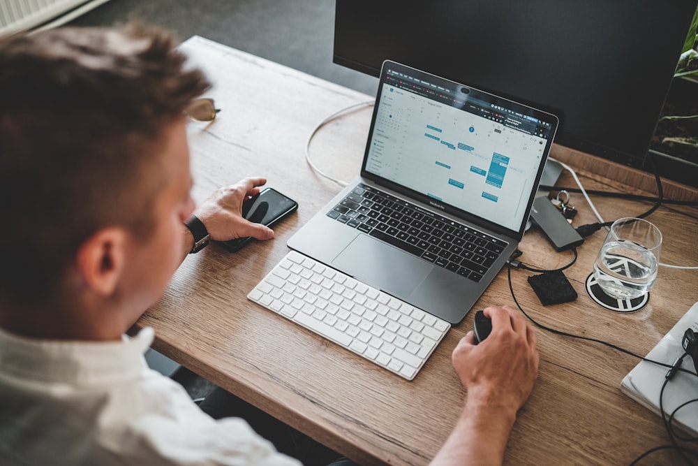 man holding mouse and iPhone while using Macbook Pro