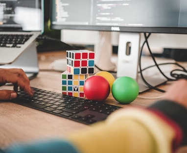 person using computer and two Rubik's Cube near monitor