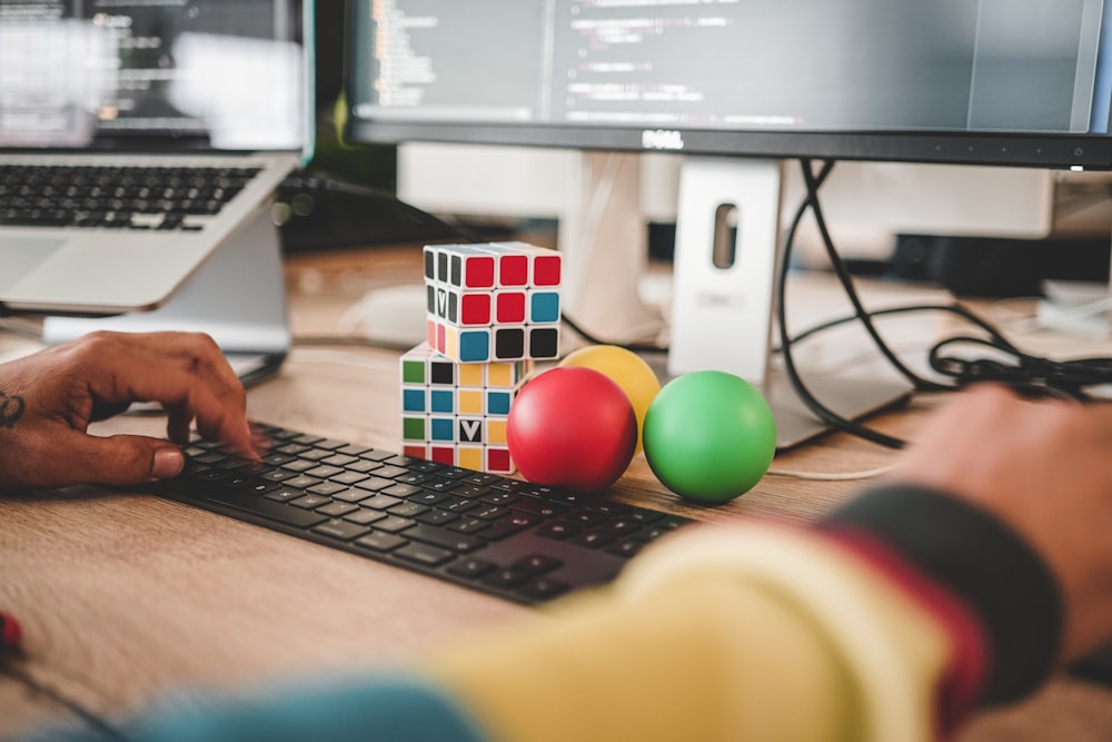 person using computer and two Rubik's Cube near monitor