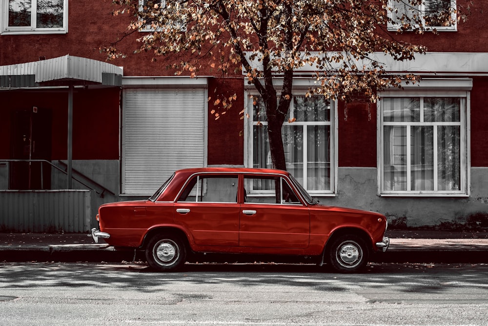 red sedan park beside tree and house