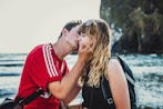 man wearing red crew-neck shirt kissing woman wearing black top