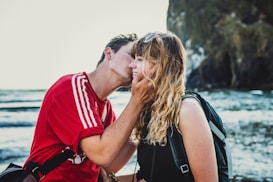 man wearing red crew-neck shirt kissing woman wearing black top
