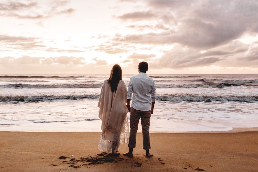 woman wearing beige dress and man wearing white dress shirt standing on seashore