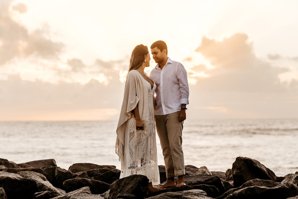 man and woman facing beside each other standing on rocky shore during day