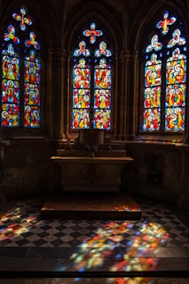 Parishioners gathered in prayer, bathed in deep red and blue hues from stained glass windows.
