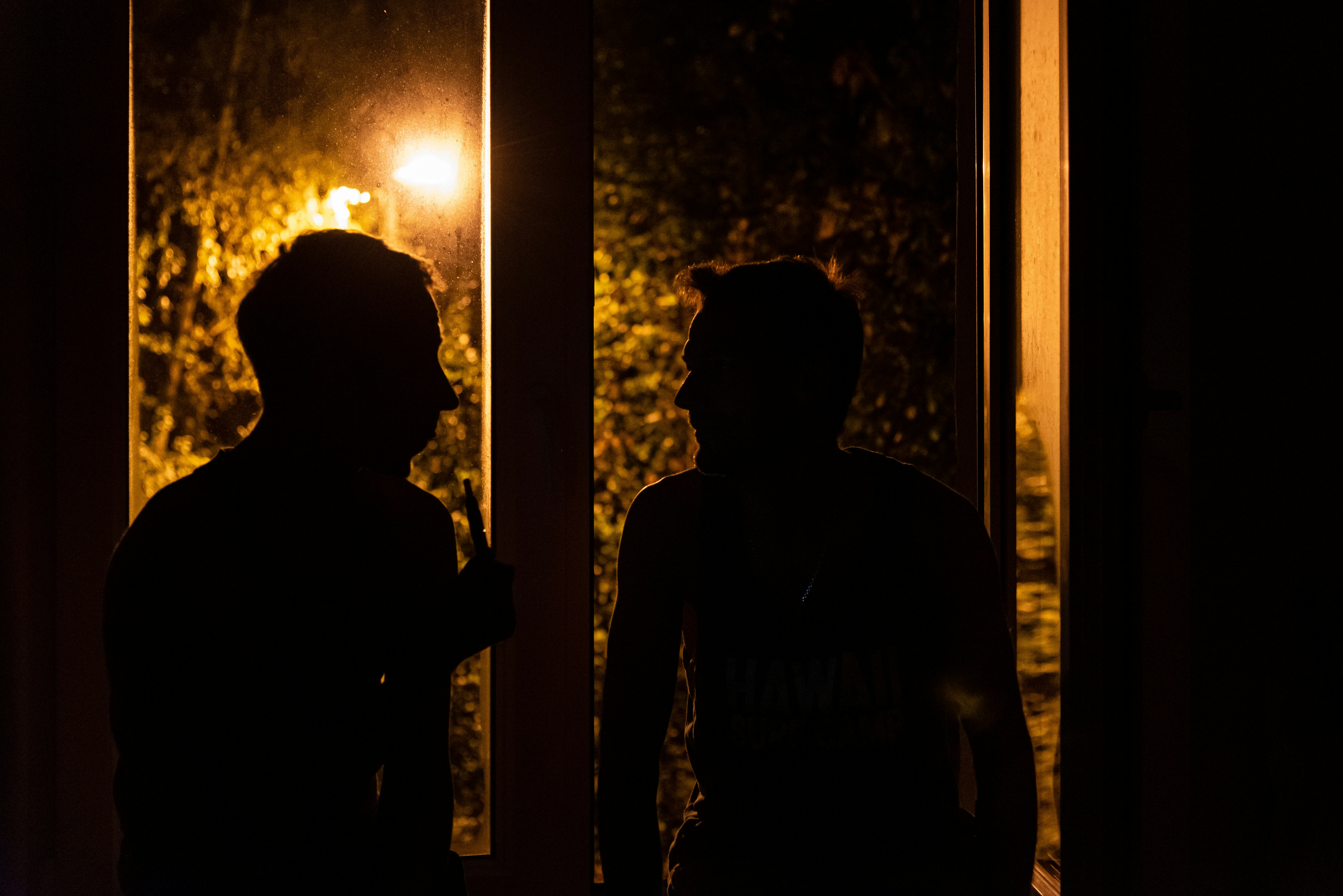 Silhouette view of two men talk to each other near window at night ...