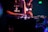 Two individuals are engaged in music mixing, with one adjusting the controls on a mixer in a dimly lit setting. The lighting is primarily purple and blue, creating a vivid nightclub atmosphere. Both are casually dressed, and one of the shirts has text printed on it.