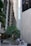 Tall skyscrapers surround a small courtyard area with palm trees. Two uniformed security personnel are conversing in the foreground. The architecture features modern and sleek designs with concrete and glass elements.