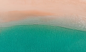 Serene aerial photo of a calm beach with clear blue water and sandy shore.