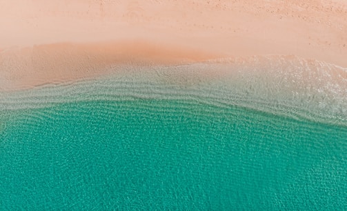 Serene aerial photo of a calm beach with clear blue water and sandy shore.