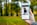 A hand holding a smartphone displaying an online shopping webpage. The screen shows a listing for a unisex sweatshirt with multiple images of a person modeling the garment. The background is a blurred scene of trees and green grass, suggesting an outdoor setting.