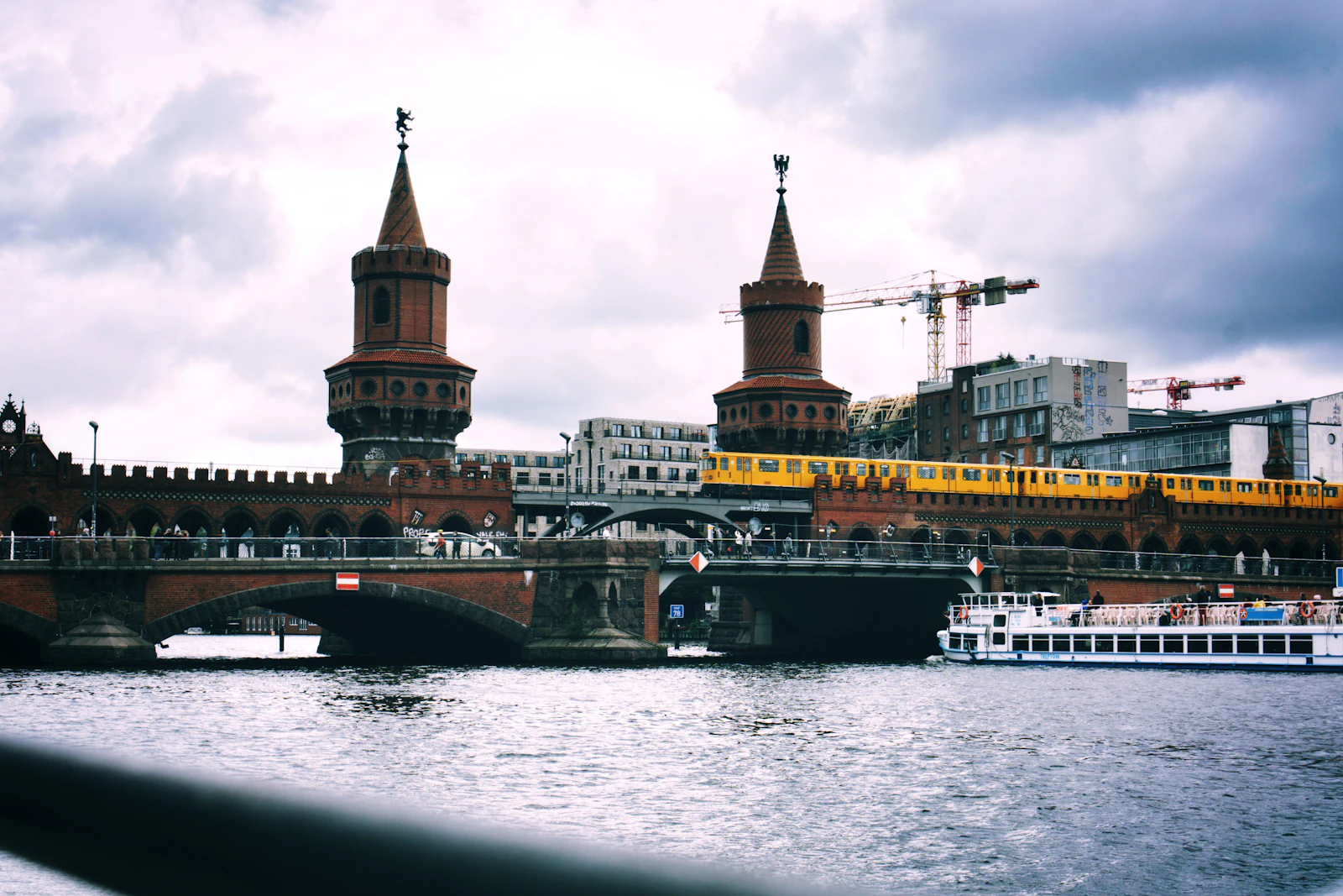Travel photograph: A yellow U-Bahn train crosses the red-brick towers of Oberbaum Bridge above the Spree.