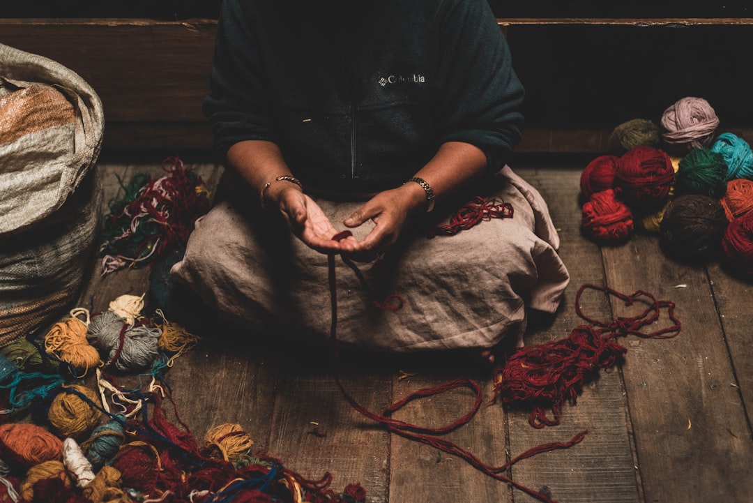 person holding red string with beige textile on lap