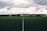 A clear, well-maintained soccer field with a central white line divides the green artificial turf. A backdrop of trees and buildings stretches across the horizon under a dramatic, cloudy sky.