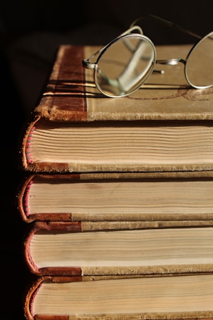 A stack of personal finance books with a pair of glasses on top, set on a wooden table with soft natural light.