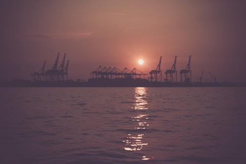 A port crane lifting containers with a sunset casting warm light over the harbor.