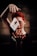 A person with red hair and freckles focuses intensely on a playing card seemingly suspended in mid-air between their raised hands. The background is dark, adding to the mysterious atmosphere.
