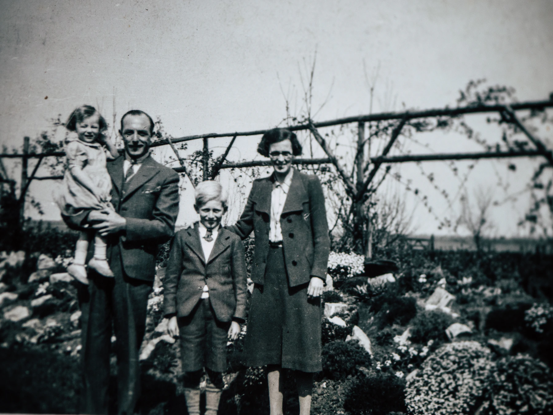 A 1930s black and white snapshot of a couple and two children standing in a garden