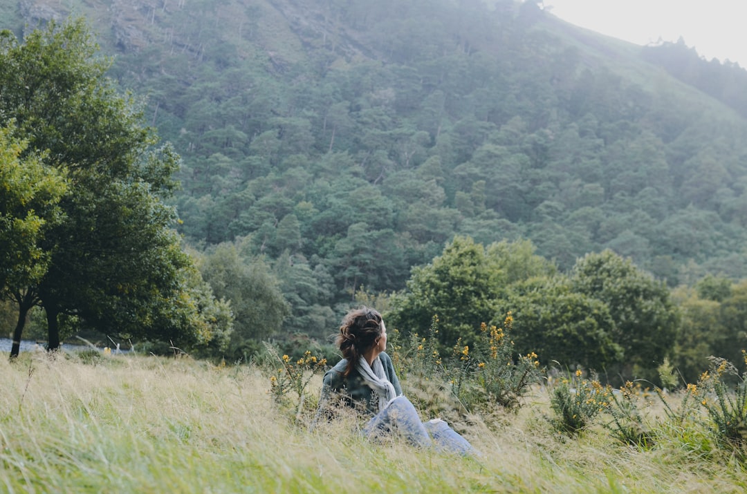 woman sitting on grass near trees, Glendalough National Park