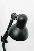 A close-up of a black, adjustable desk lamp with a rounded head and multiple hinges on the arm.