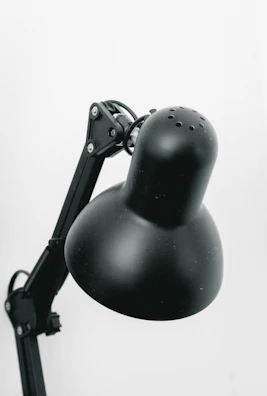 A close-up of a black, adjustable desk lamp with a rounded head and multiple hinges on the arm.