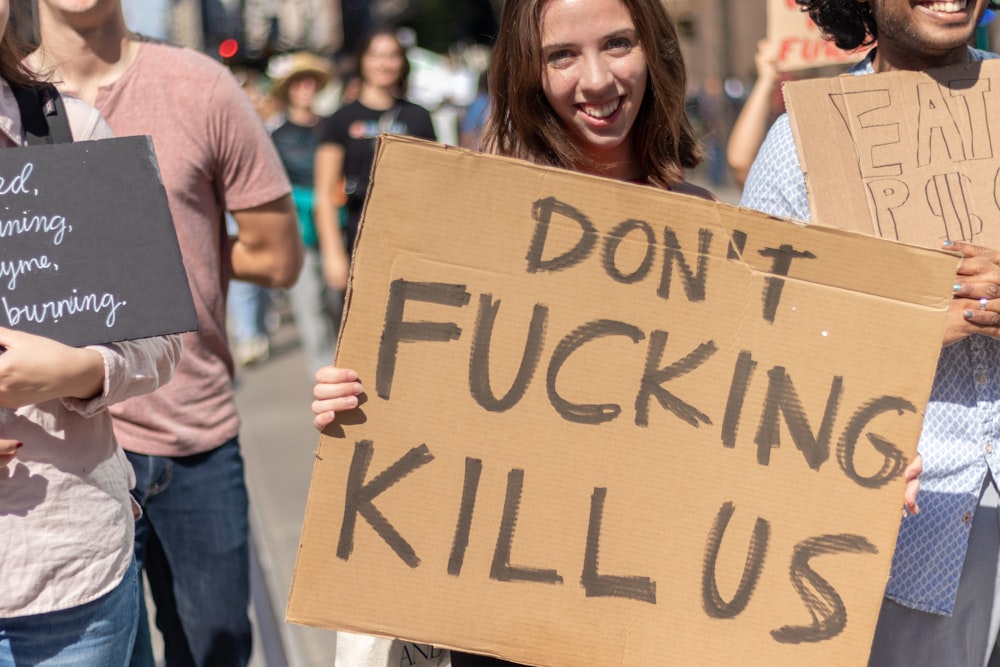 smiling woman holding Don't Fucking Kill Us sign