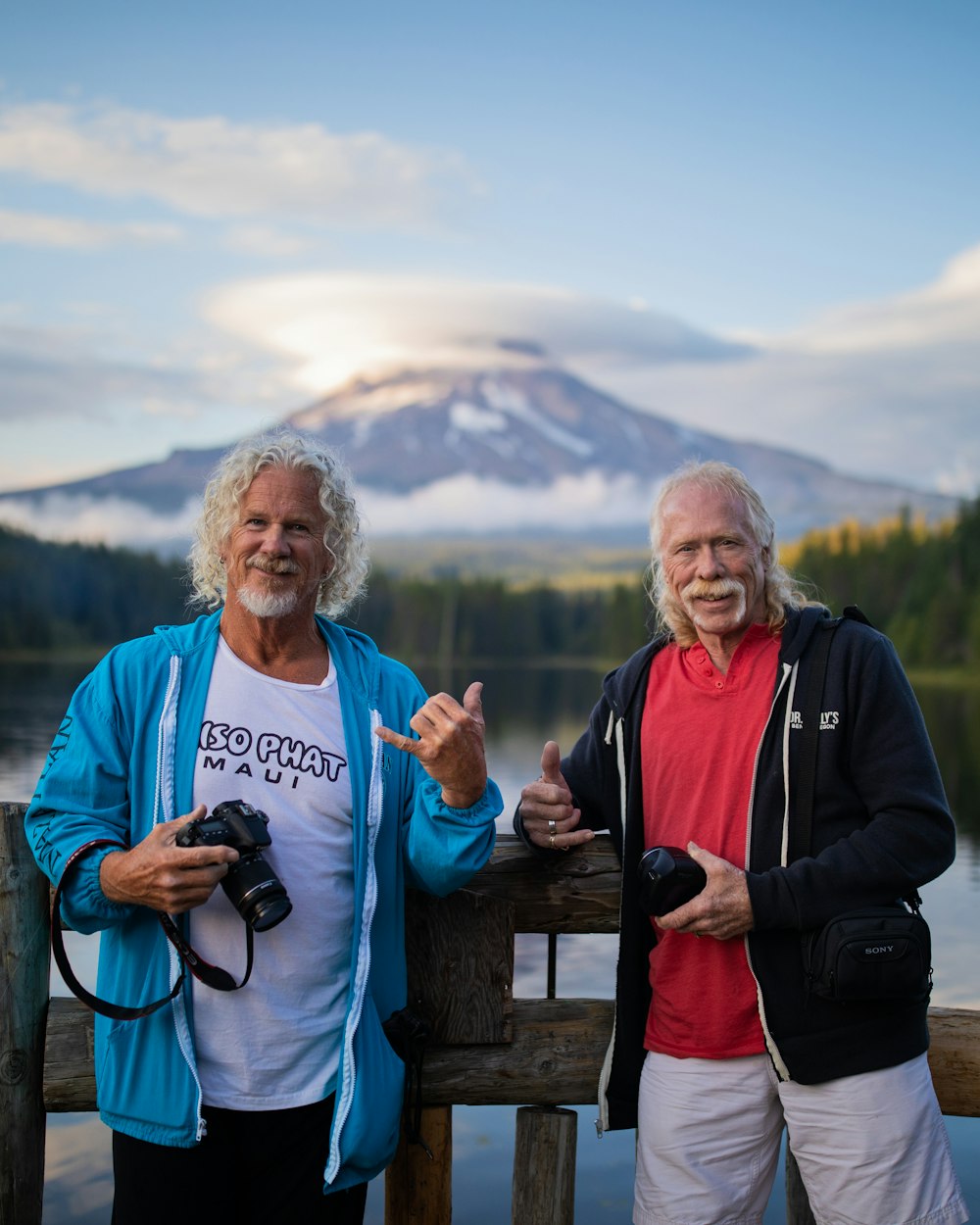 two mean holding cameras while leaning on railings by the lake