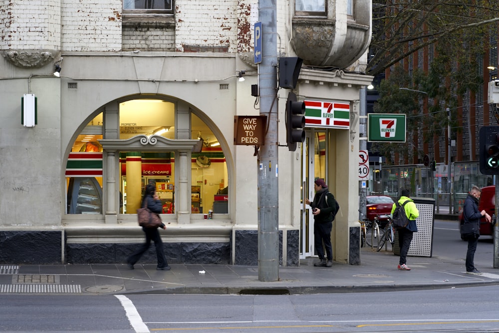 four people walking on sidewalk beside 7-eleven