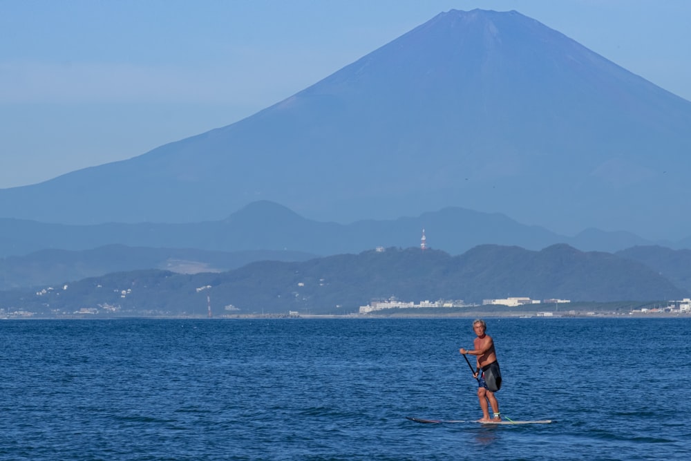 hombre con una tabla de surf y una montaña al fondo