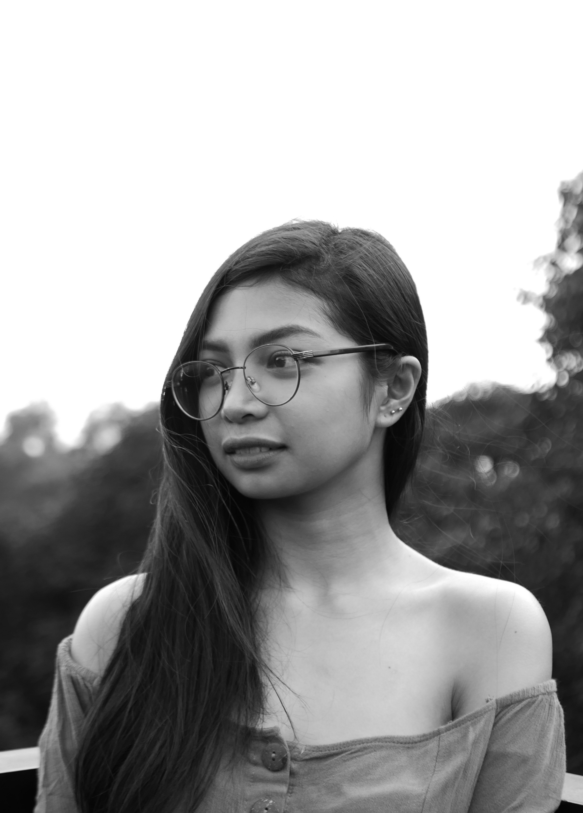 Photographie en niveaux de gris d’une femme portant un chemisier à épaules dénudées et des lunettes souriant tout en jetant un coup d’œil à son côté droit